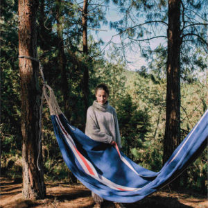 A woman is in the forest with a handmade hammock from Colombia in blue, white, red colors