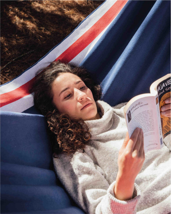 A woman is lying in a Paris hammock reading a book