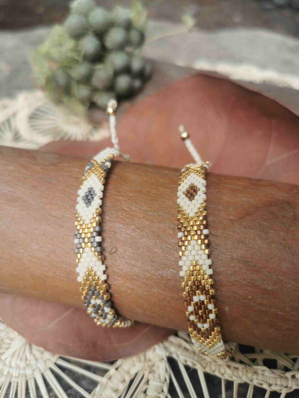 Une paire de bracelets artisanaux de Colombie tissée à la main avec des perles dorées, blanches, grises et marrons posée sur un fond naturel.